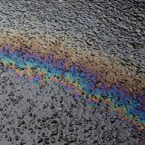 Iridescent oil slick on a dark, textured surface.