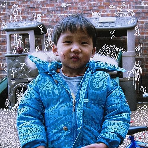 A young boy in a blue patterned jacket stands in front of a playground.