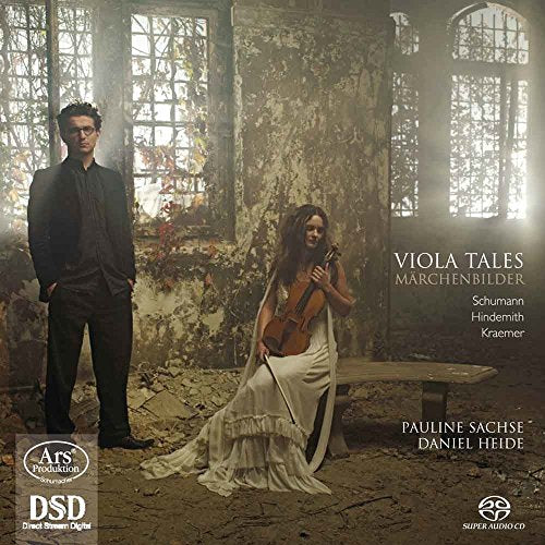 A man in a suit and a woman with a viola stand in ruins.