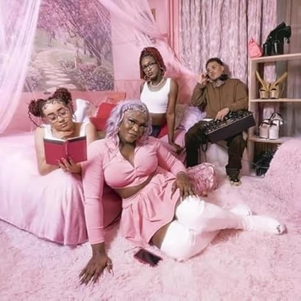 Three people relax on a pink bed and furniture, surrounded by pink.