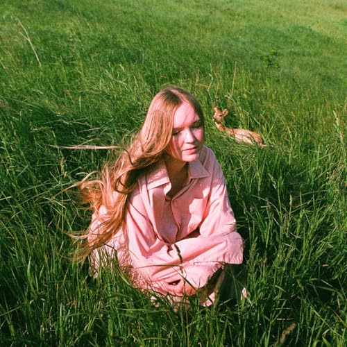 Woman with long hair in a pink shirt sits in tall green grass.