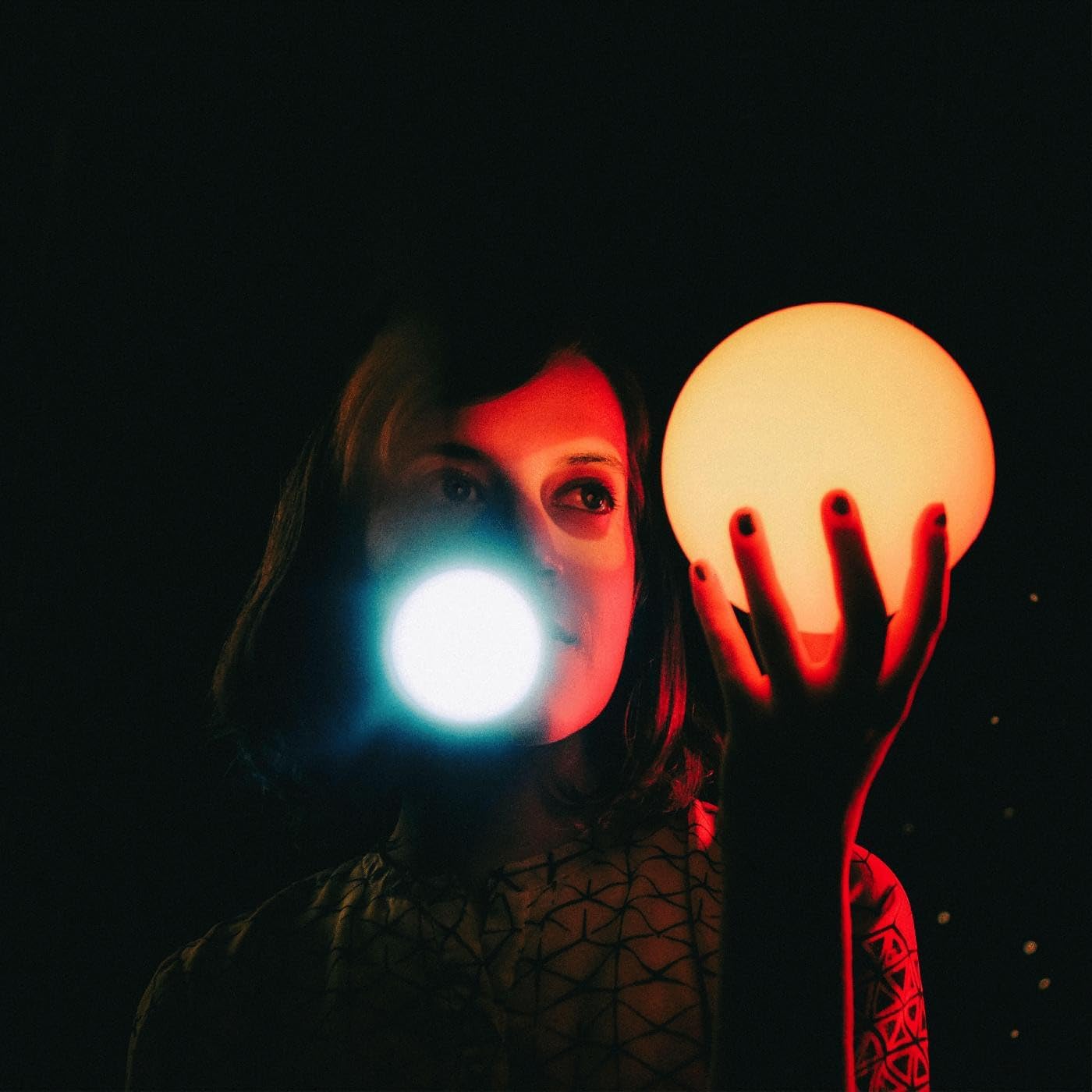 A person in dark lighting holds a glowing orb, with a bright light near them.
