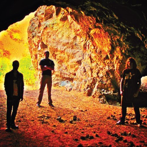 Three people stand before a large, illuminated rock formation.