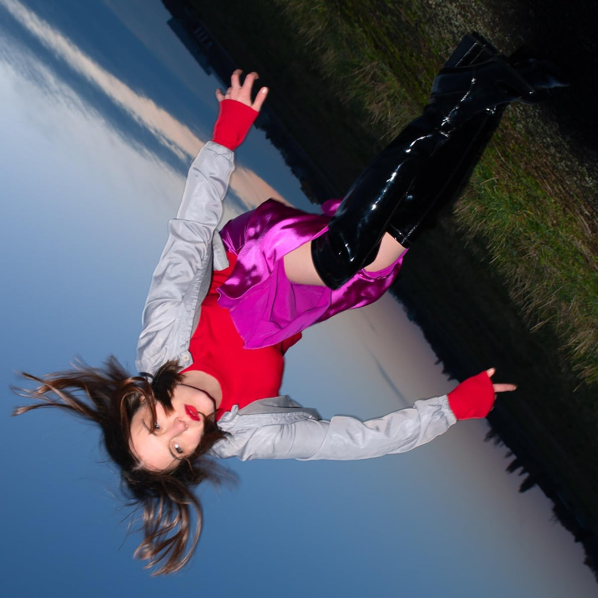 Woman in red and pink outfit poses dynamically against a blue sky.