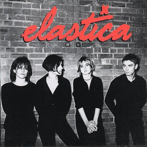 Black and white photo of four people, the band Elastica, against a brick wall.