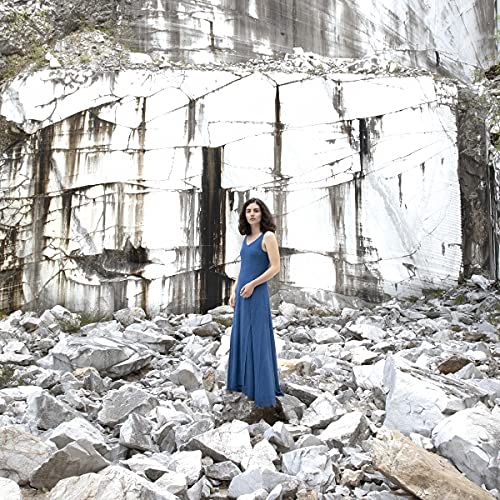 Woman in blue dress stands among rocks before a stone quarry.