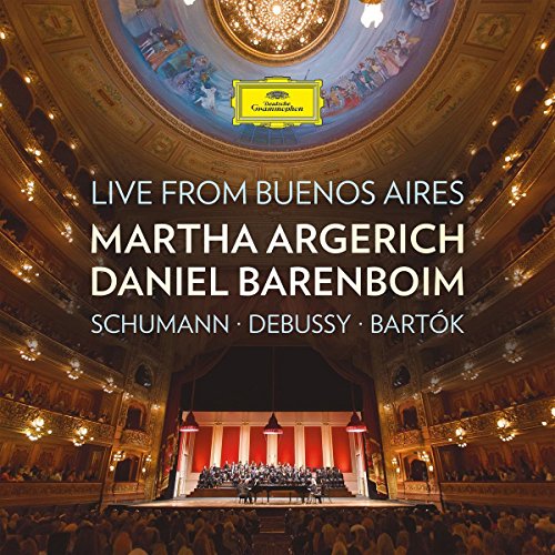 Classical musicians performing on ornate stage in crowded concert hall with high ceiling.