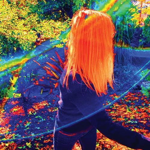 Woman with bright orange hair seen from behind in a colorful garden.