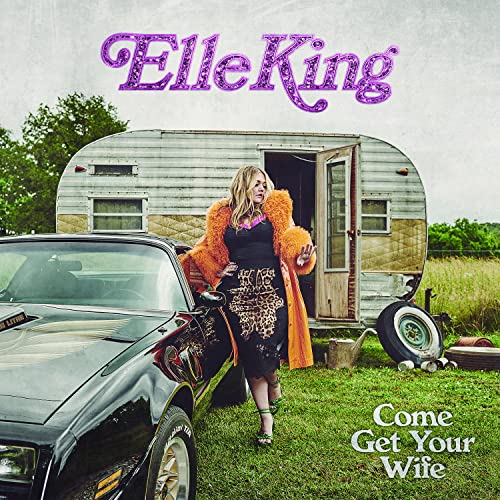 Elle King poses by a car and vintage trailer on grass.