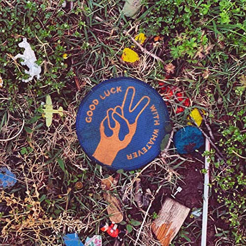 CD with hand-making-peace-sign design lying in green grass and debris.