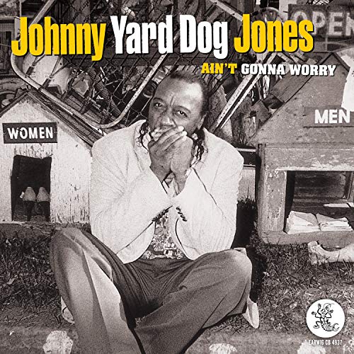 Johnny Yard Dog Jones playing harmonica in front of dog houses labeled Women and Men.