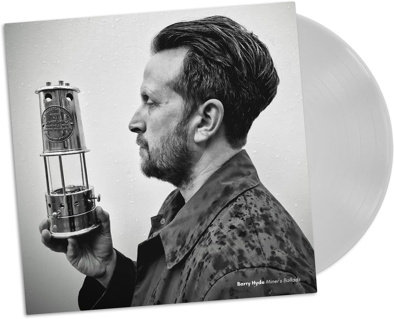 Black and white portrait of a man holding a miner’s lamp, vinyl record beside.
