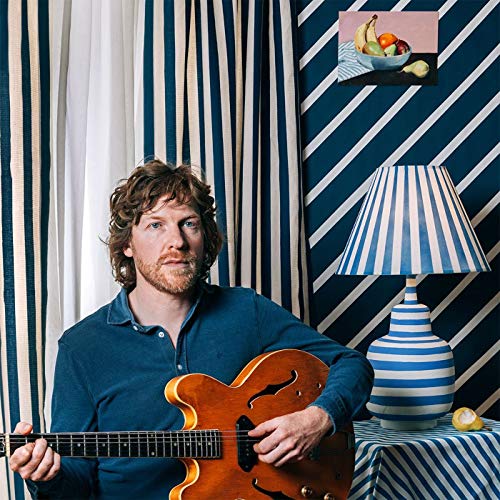 Doug Paisley holding a guitar in front of striped wallpaper.