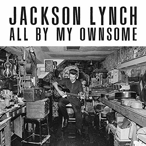 Black and white album cover featuring a man playing guitar in a cluttered room.