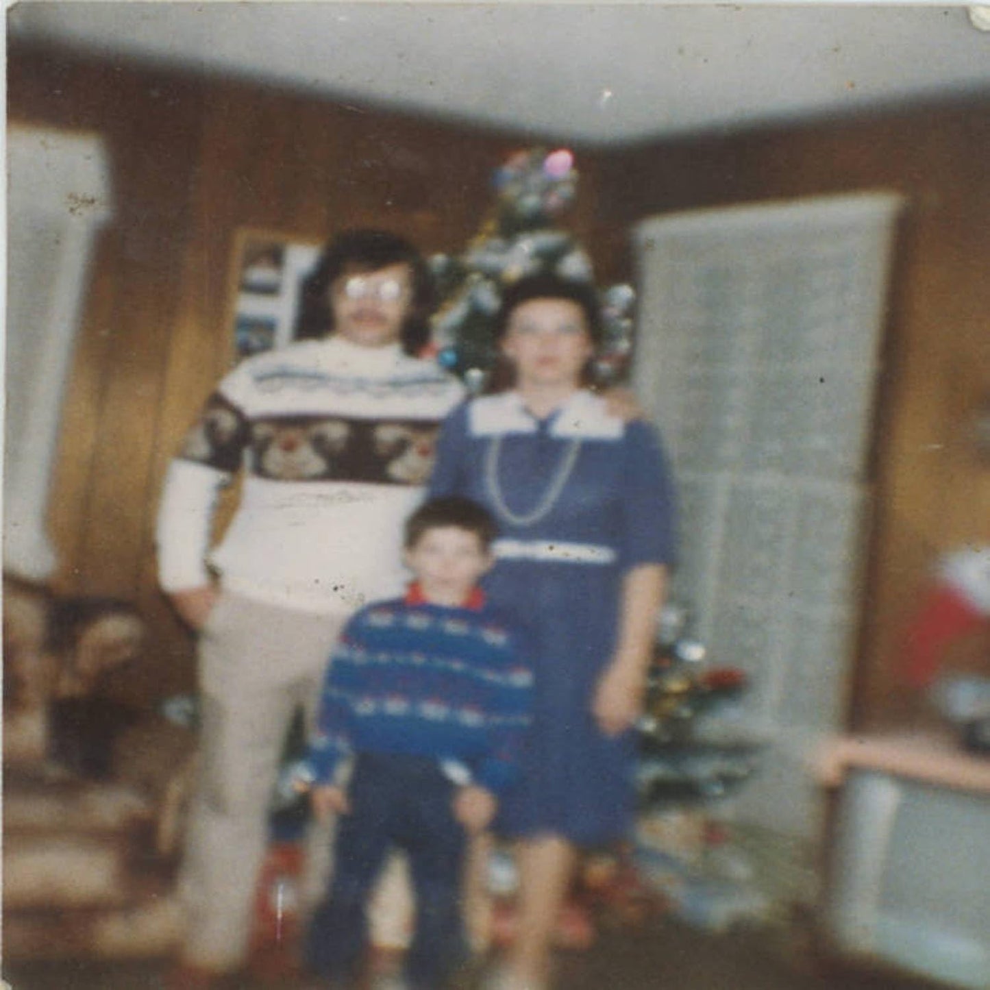 Faded photo of a family of three posing in front of a Christmas tree.