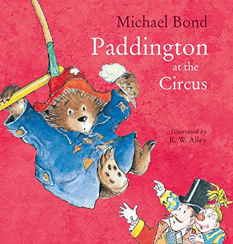 Paddington Bear in a blue coat and red hat swinging from a circus trapeze.
