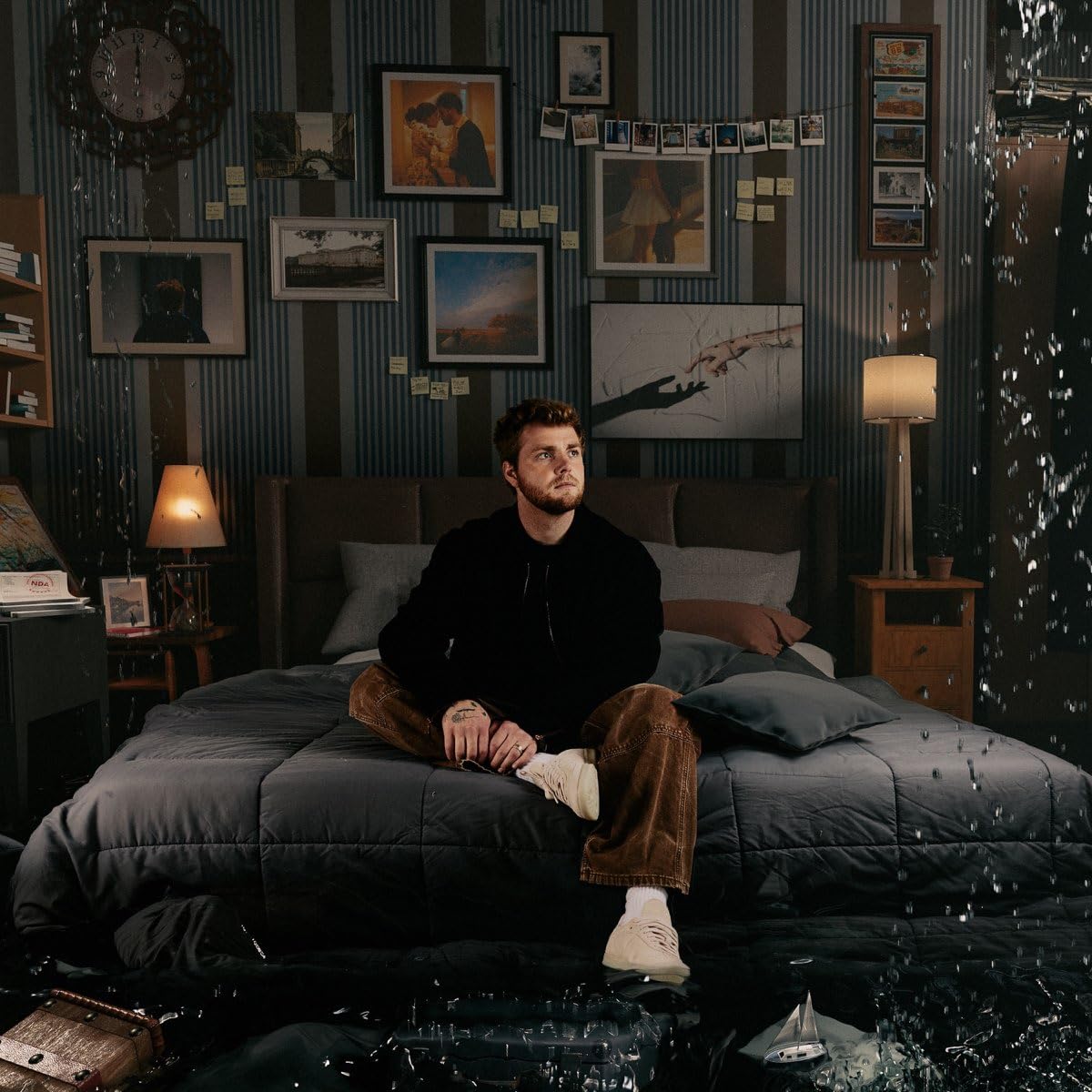 Man sitting on bed in room with many framed photos.