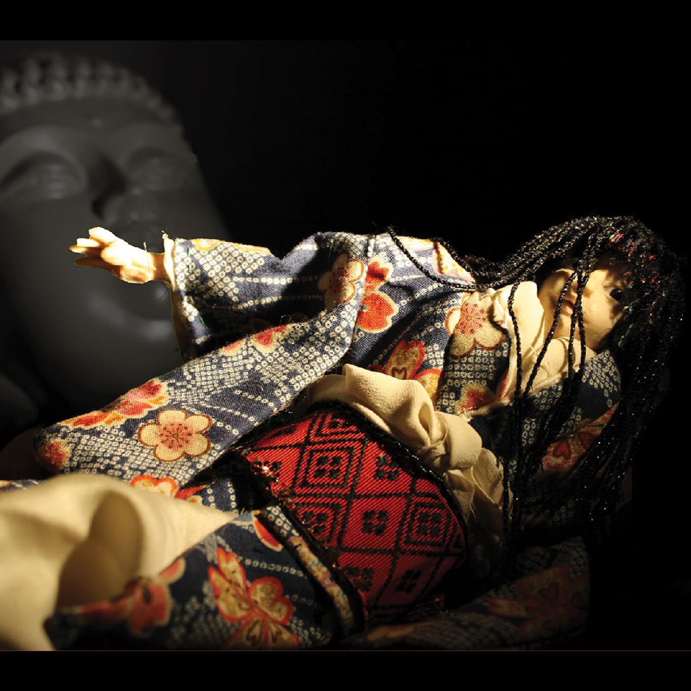 Doll in patterned kimono lies dramatically lit against a dark background.