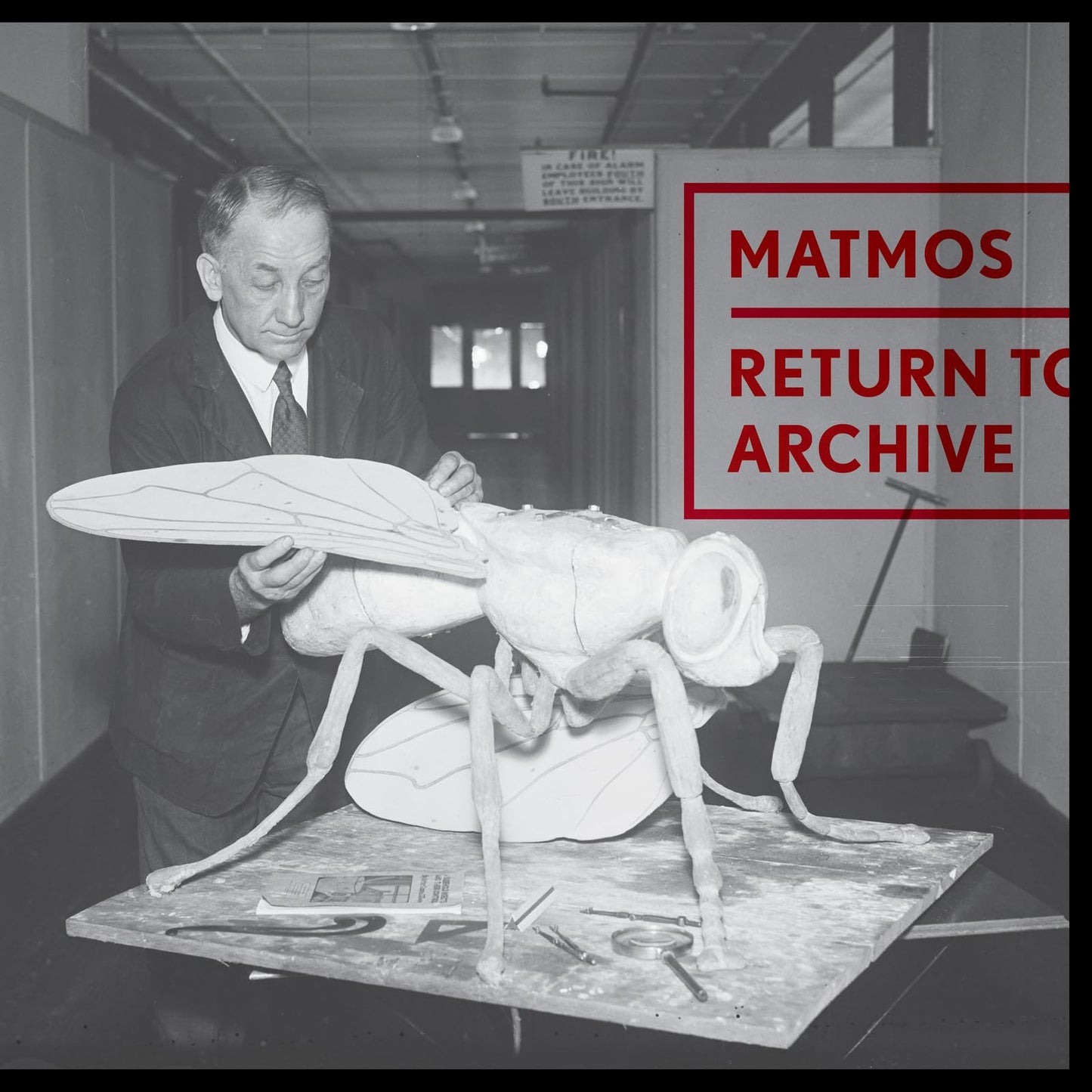 Black and white photo of a man with a large insect sculpture.