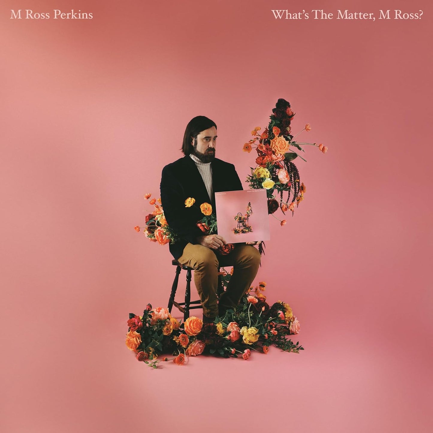 Man sitting with flowers and vinyl record against a pink background.