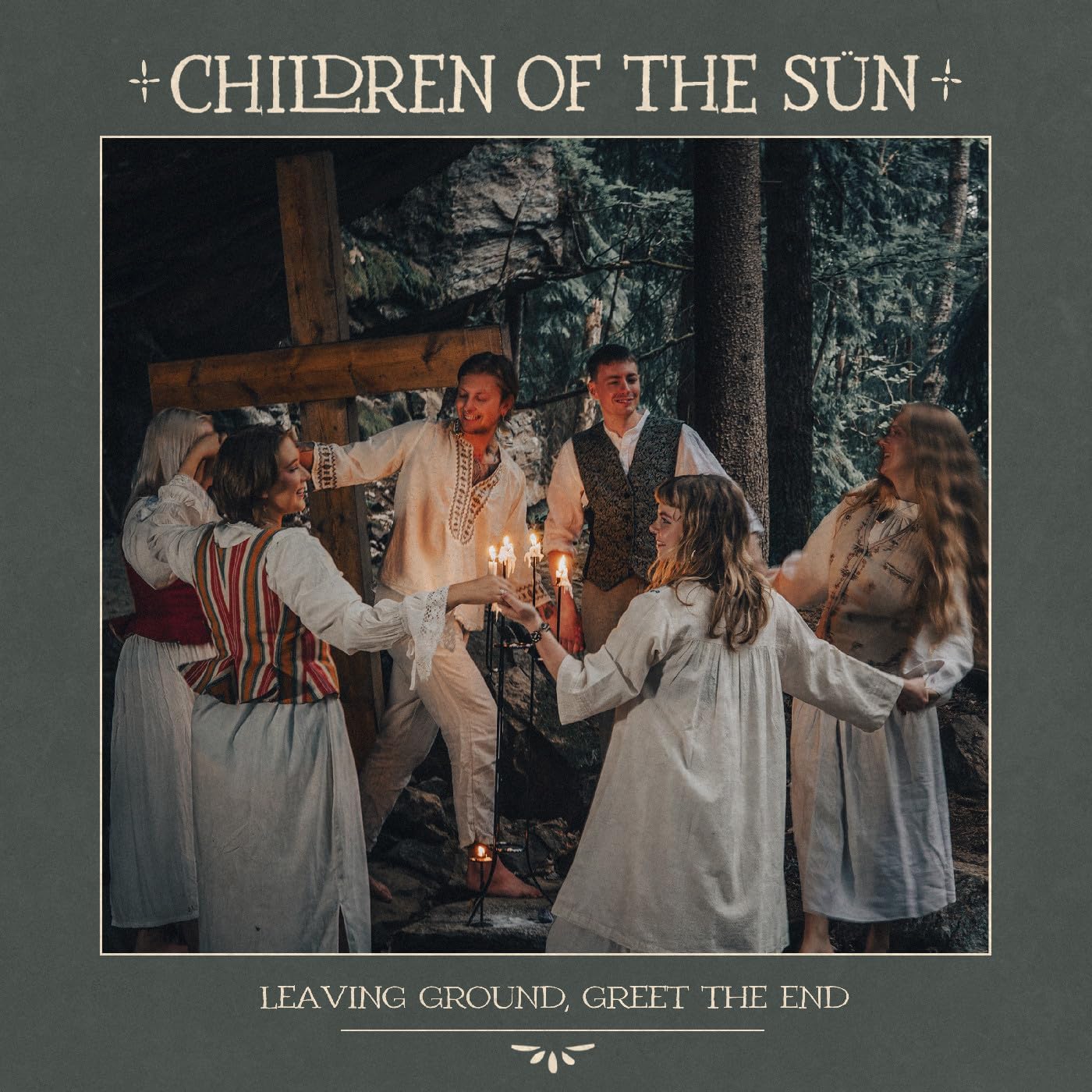 People in folk clothing hold candles in a forest clearing.