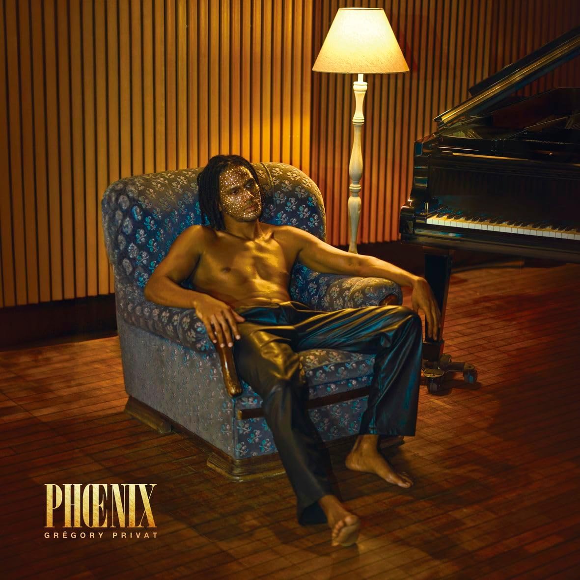 Man with glitter on face sits in blue chair by piano.