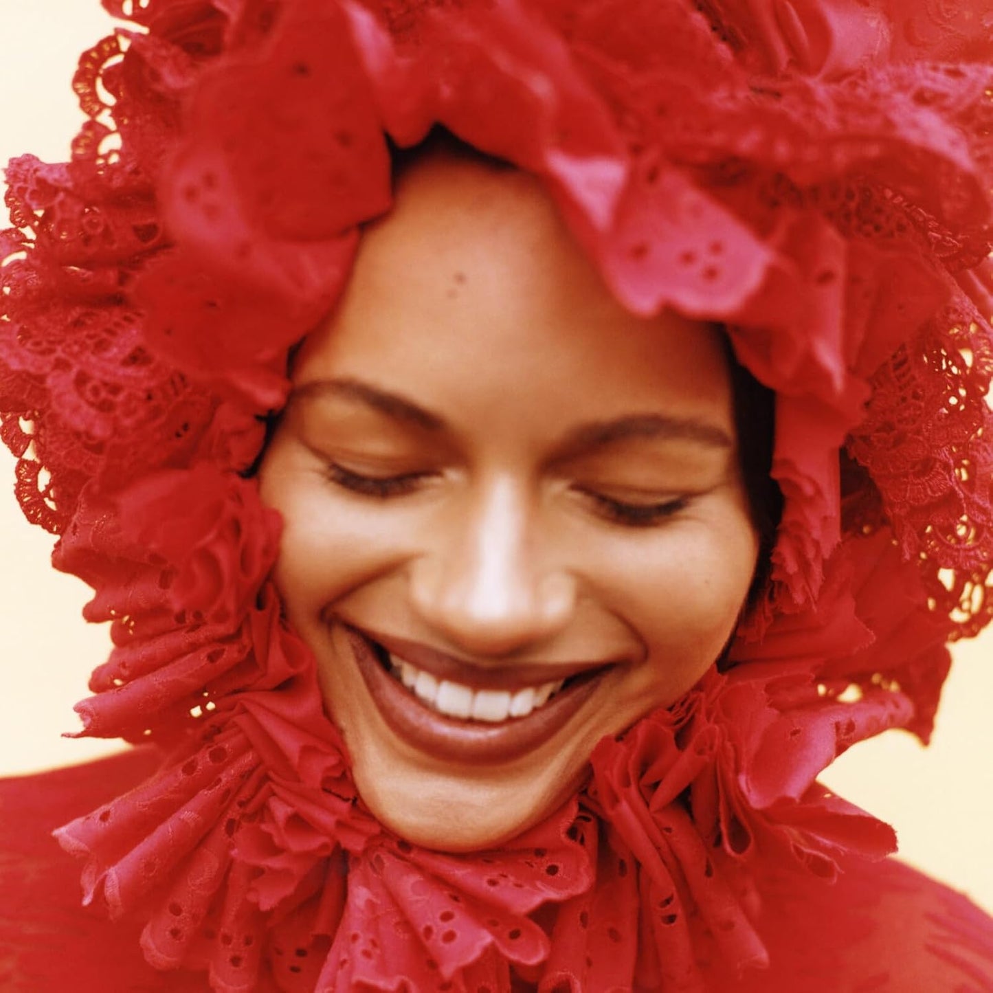 Close-up of a smiling woman wearing a large, ruffled red headpiece.
