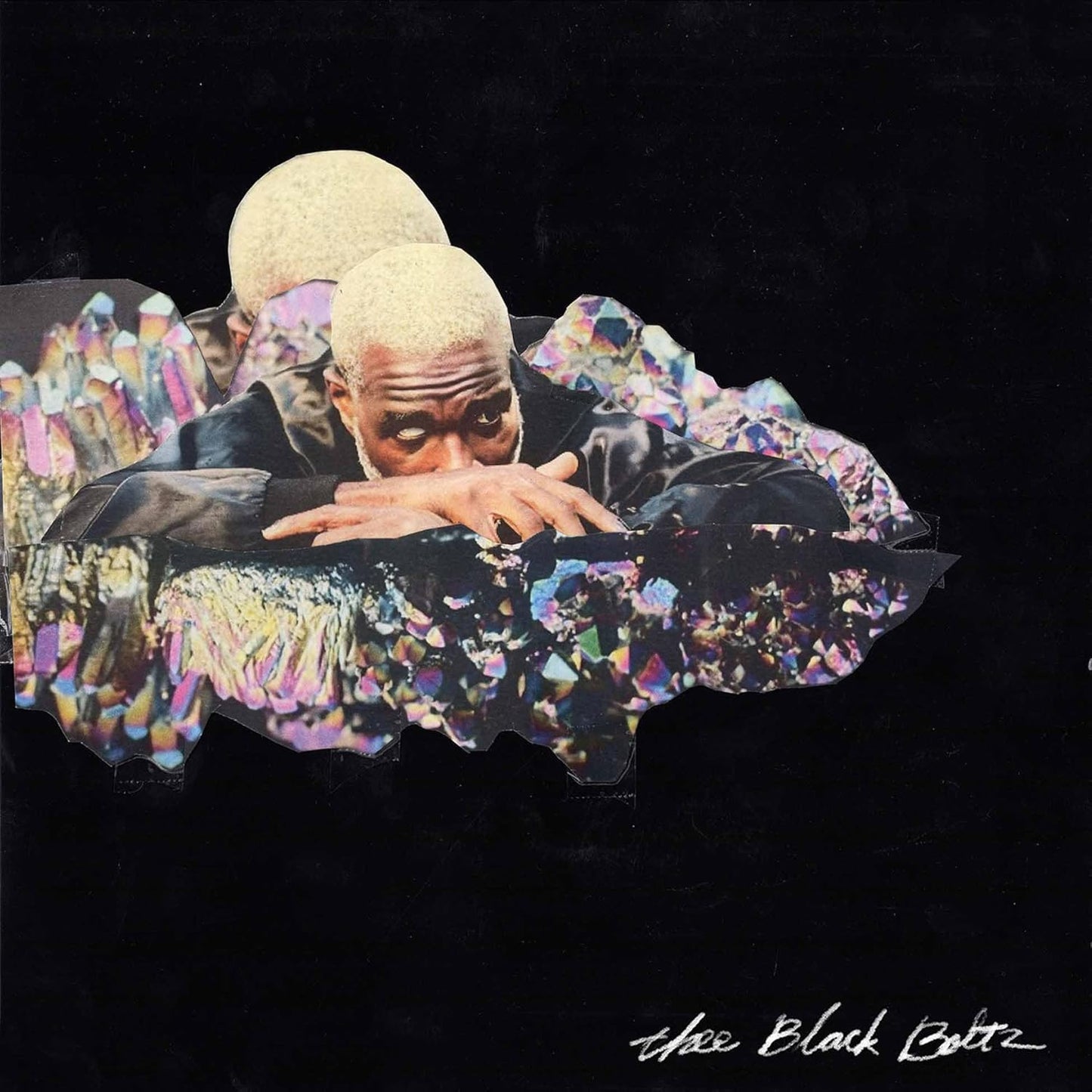 Man with bleached hair peering over iridescent crystals against a black background.