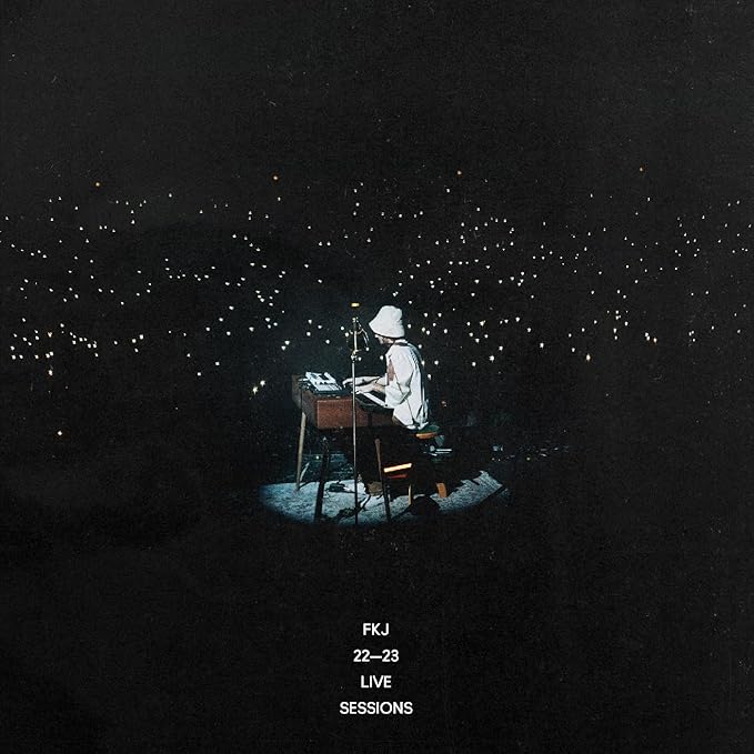 Musician at a keyboard illuminated by a spotlight, dark background.