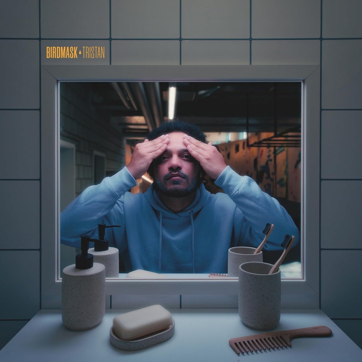 Man with hands on forehead framed by a bathroom mirror and toiletries.