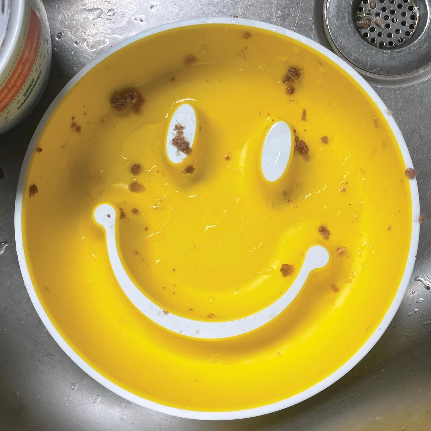 Yellow plate with a smiley face made of crumbs and liquid.
