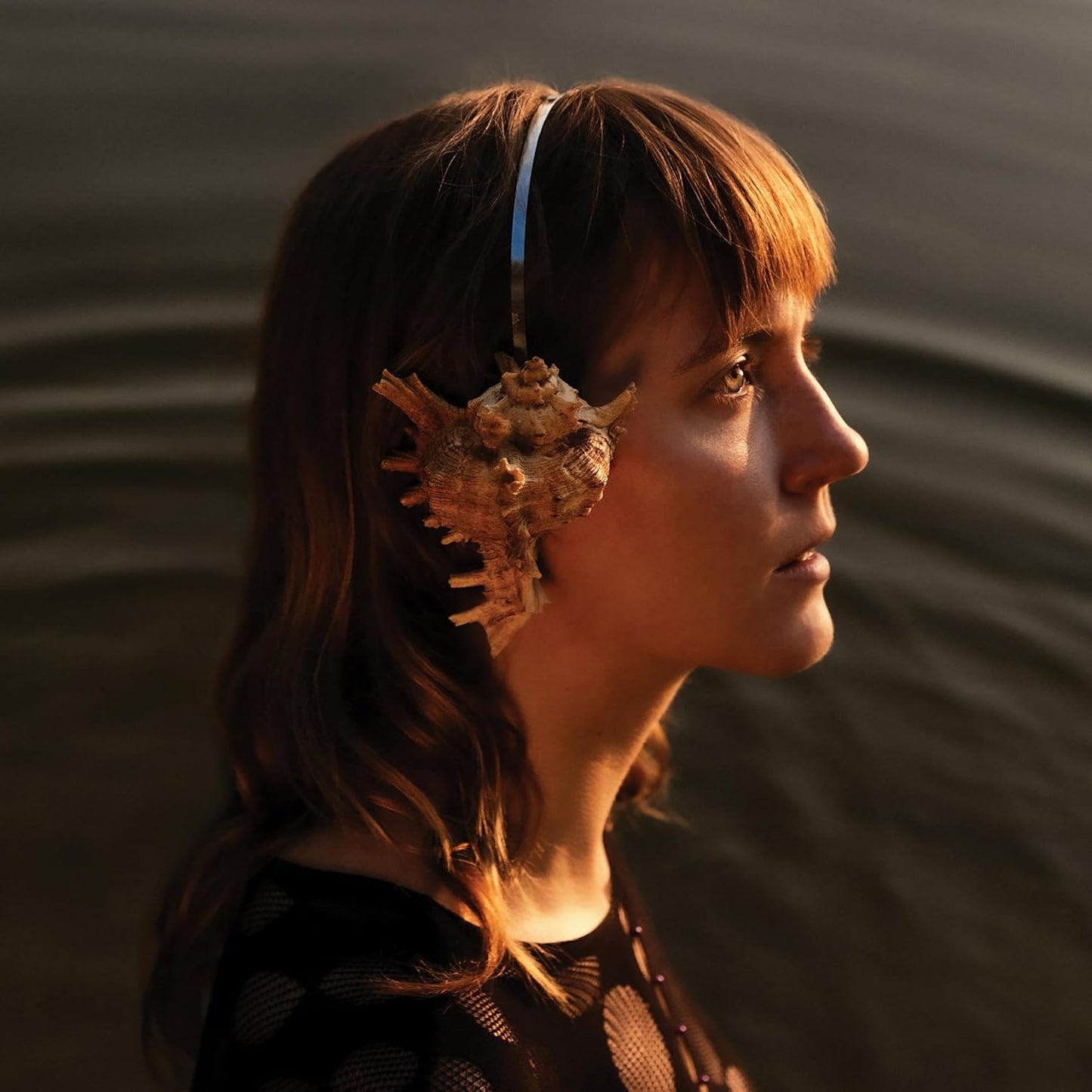 Woman in profile wearing large seashell earrings, warm lighting.