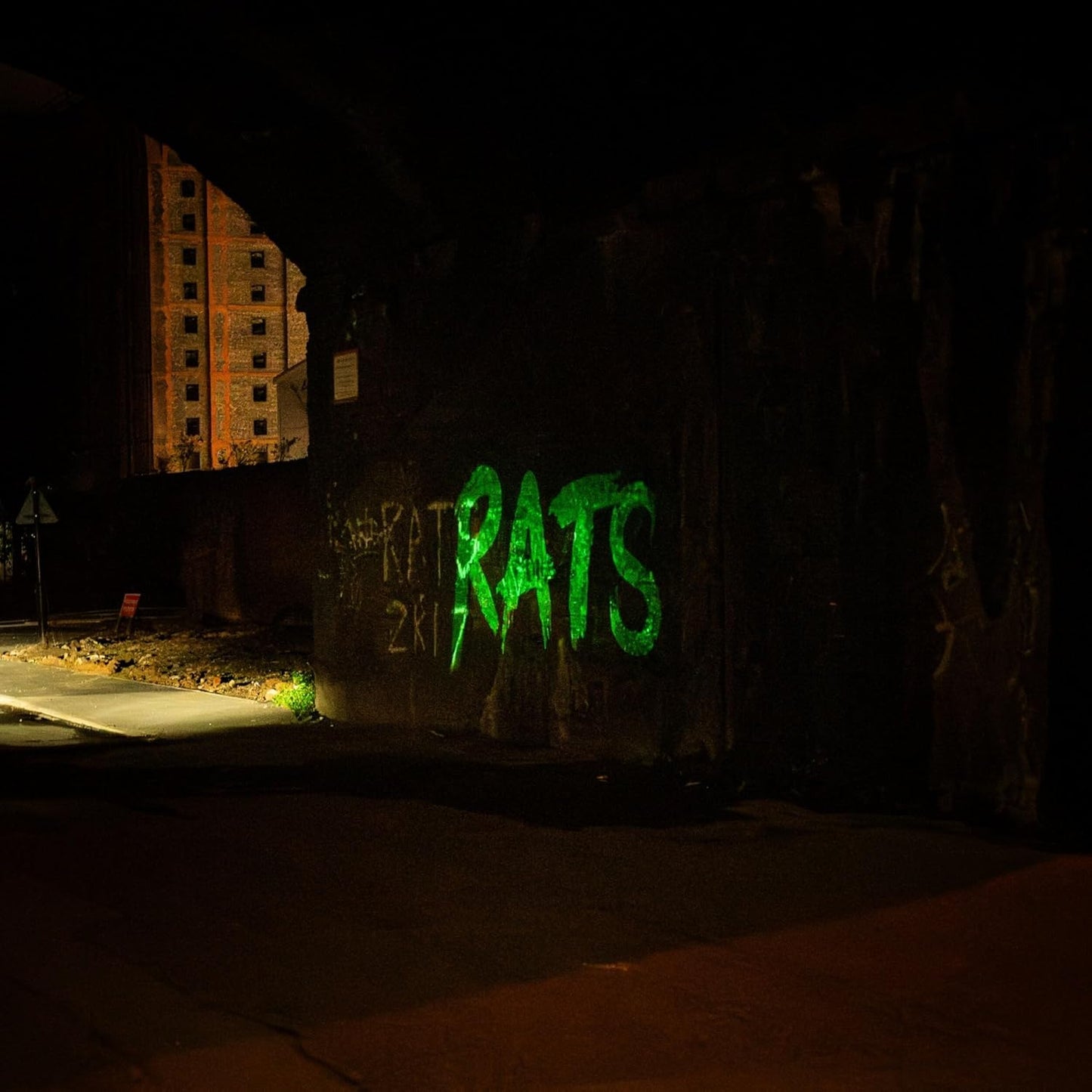 Nighttime graffiti of the word "RATS" in bright green paint on a wall.