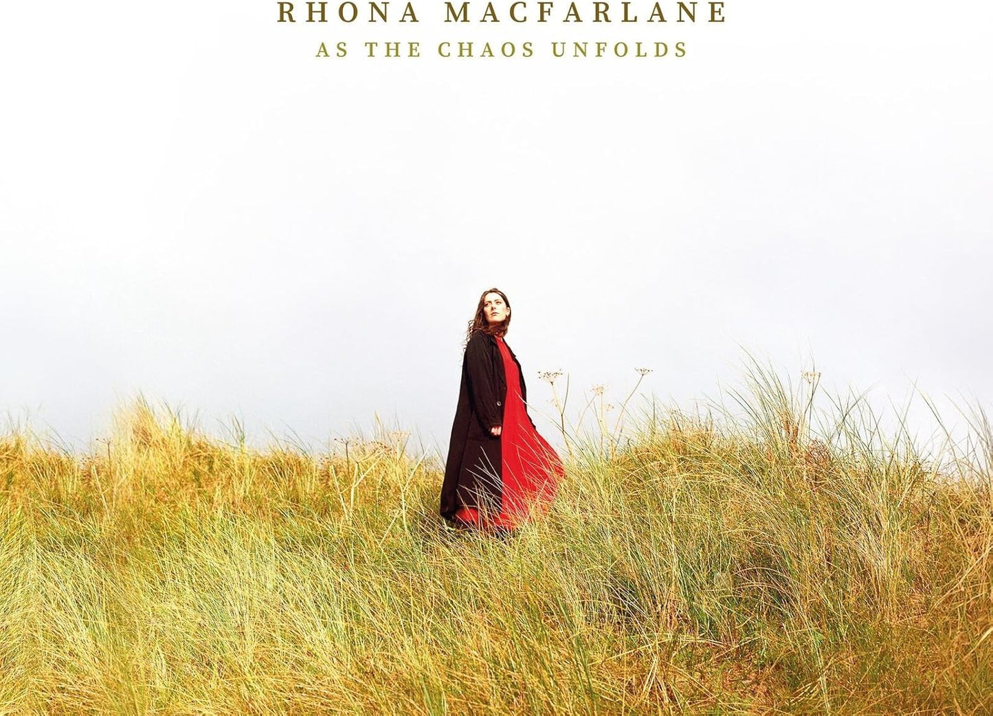 Woman in red and black standing in a field of tall grass.