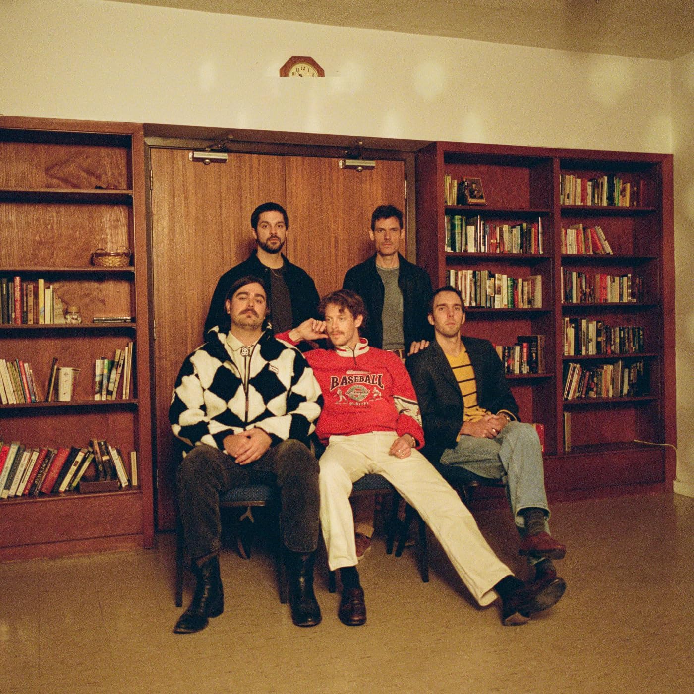 Caamp band portrait, five men seated in front of bookshelves.
