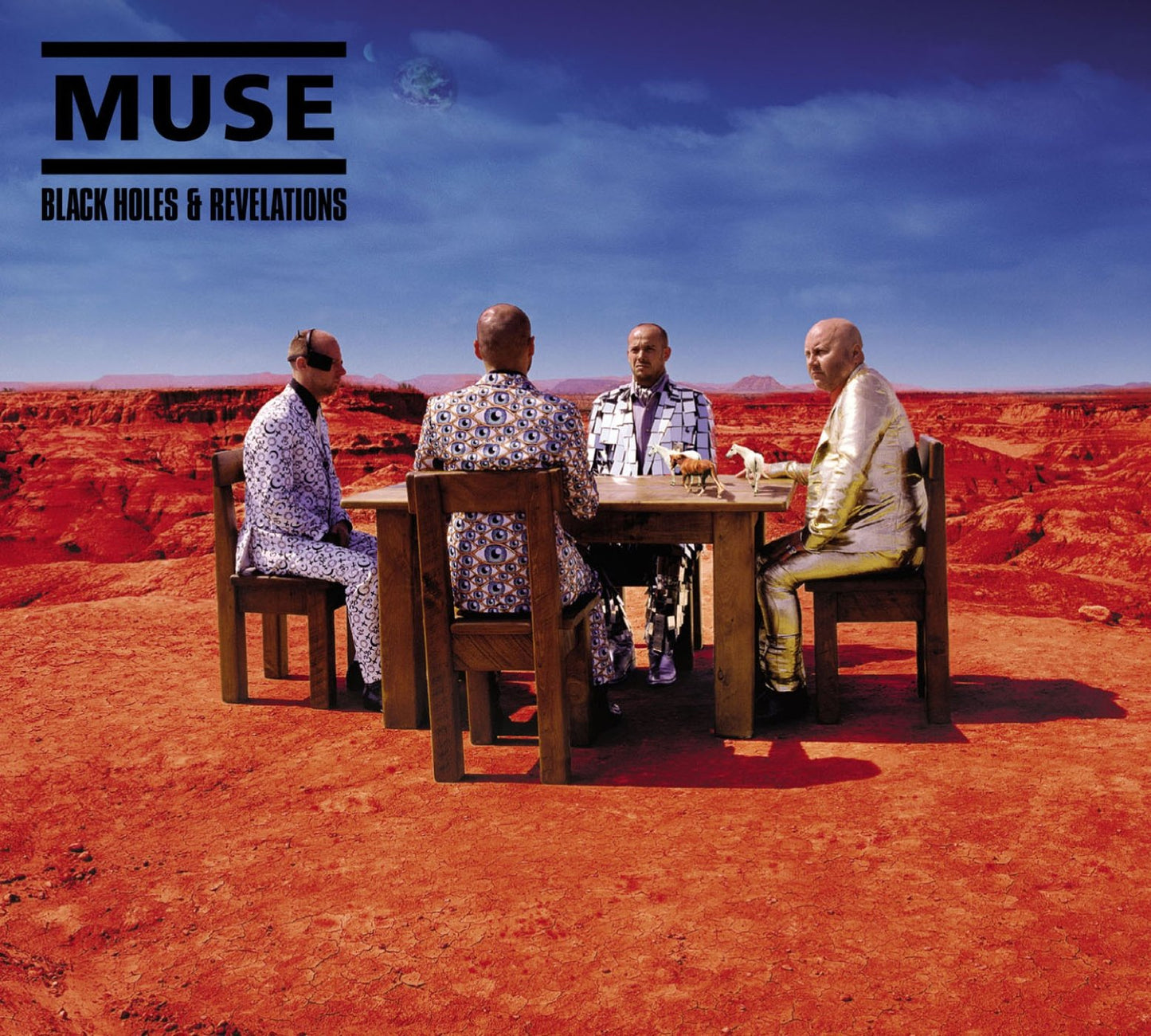 Four people seated around a table in a desert landscape.