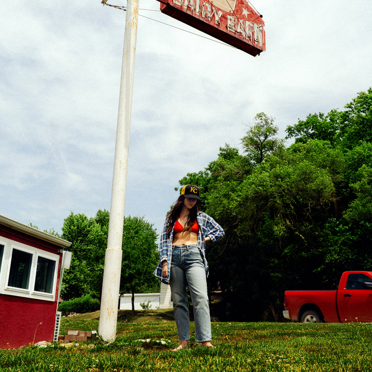 Woman in plaid shirt and hat standing in front of a sign.