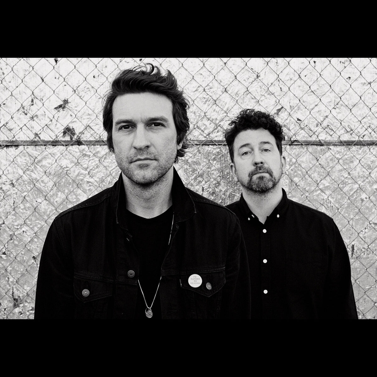 Black and white portrait of two men, Japandroids band members, against chain-link.
