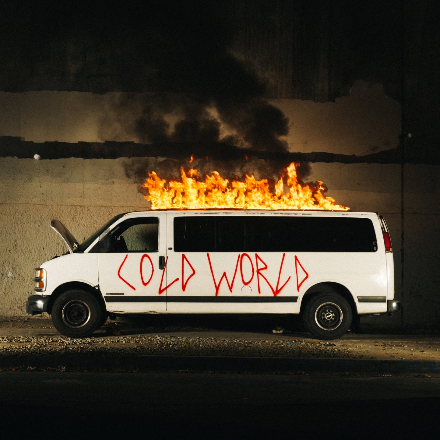 White van with “Cold World” graffiti, engulfed in flames, nighttime setting.