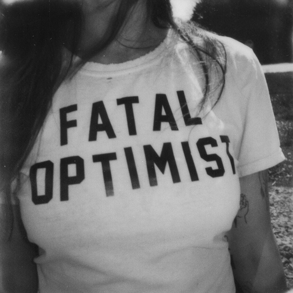 Black and white photo of a person wearing a shirt that says "Fatal Optimist".