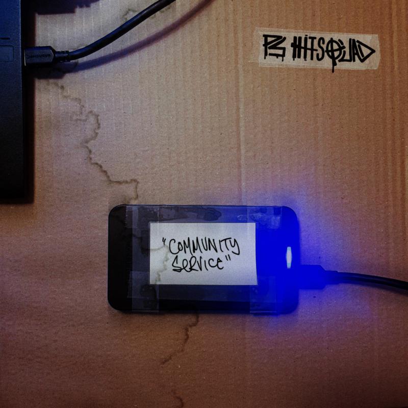 CD case with handwritten title "Community Service" resting on cardboard.