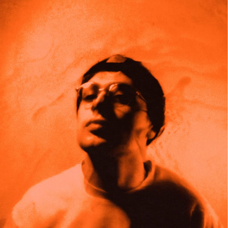 Close-up of a person wearing sunglasses, bathed in orange light.