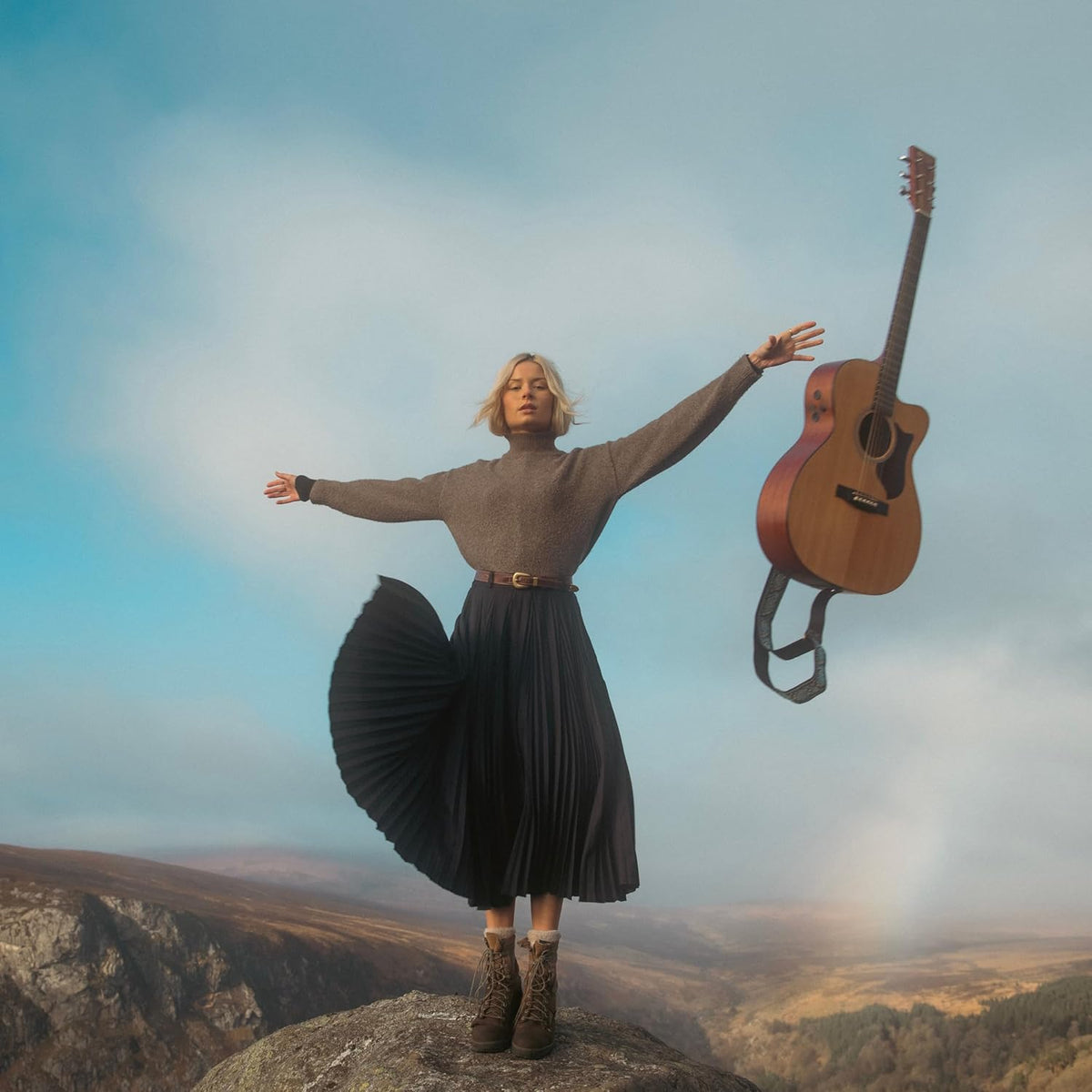 Woman with arms raised and a floating acoustic guitar outdoors.