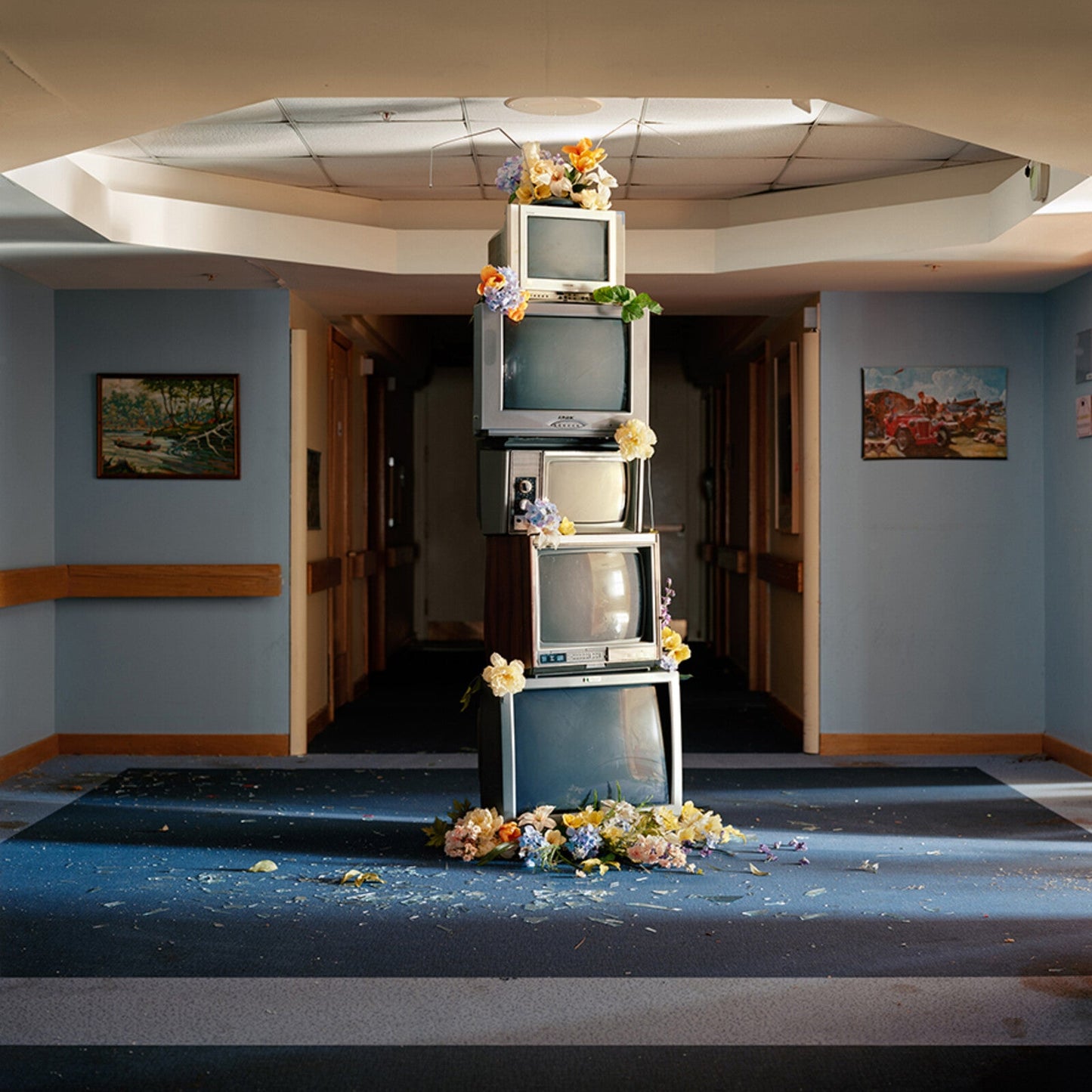 Stacked vintage televisions adorned with flowers in a blue hallway.