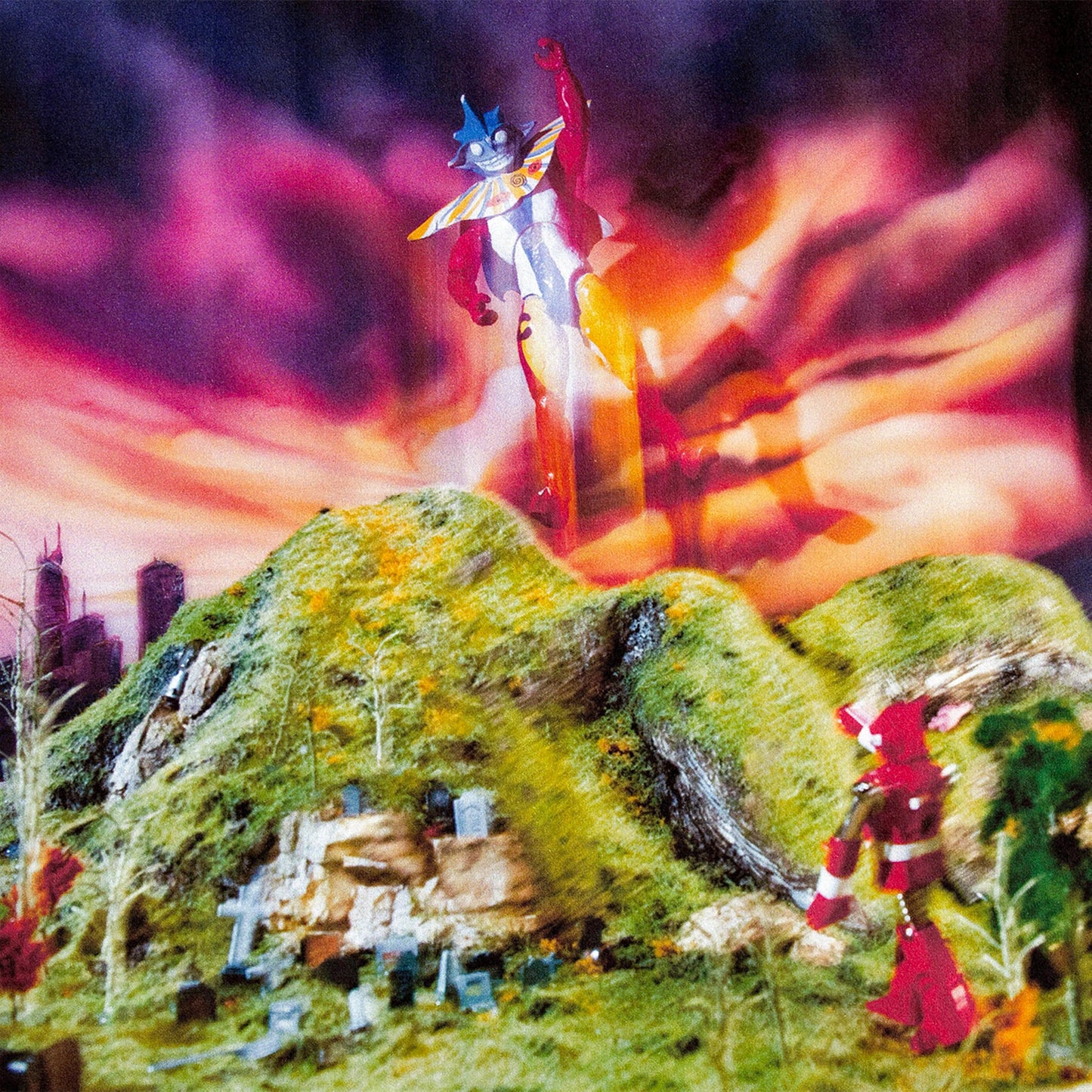 Two colorful robot figures stand on a miniature landscape with a city.