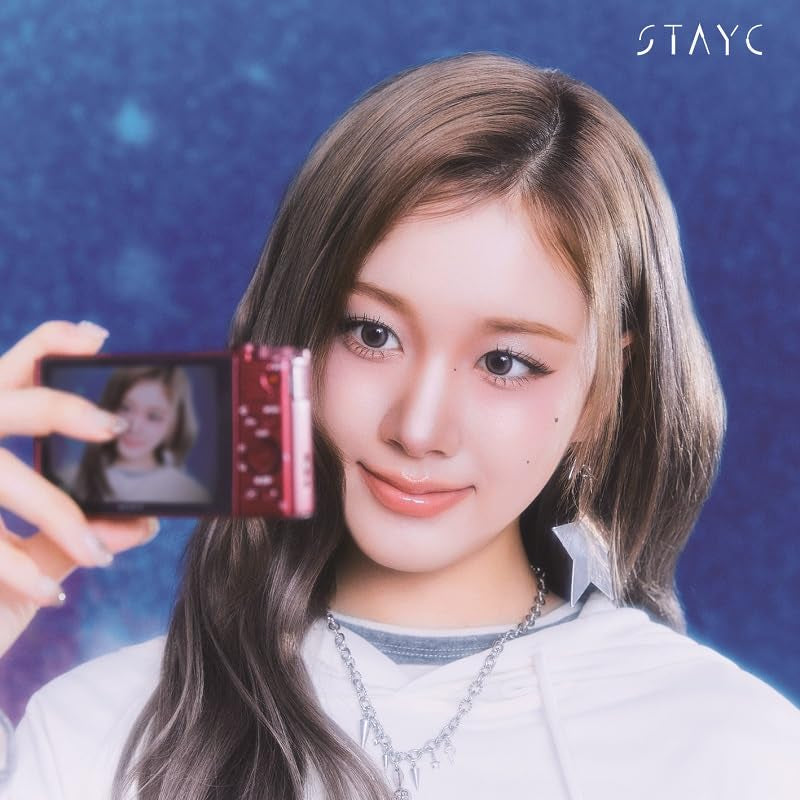 Stayc member holding a phone displaying another person, blue background.