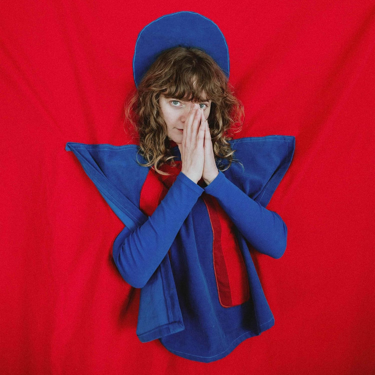 Person with curly hair in blue and red clothing, hands covering face.