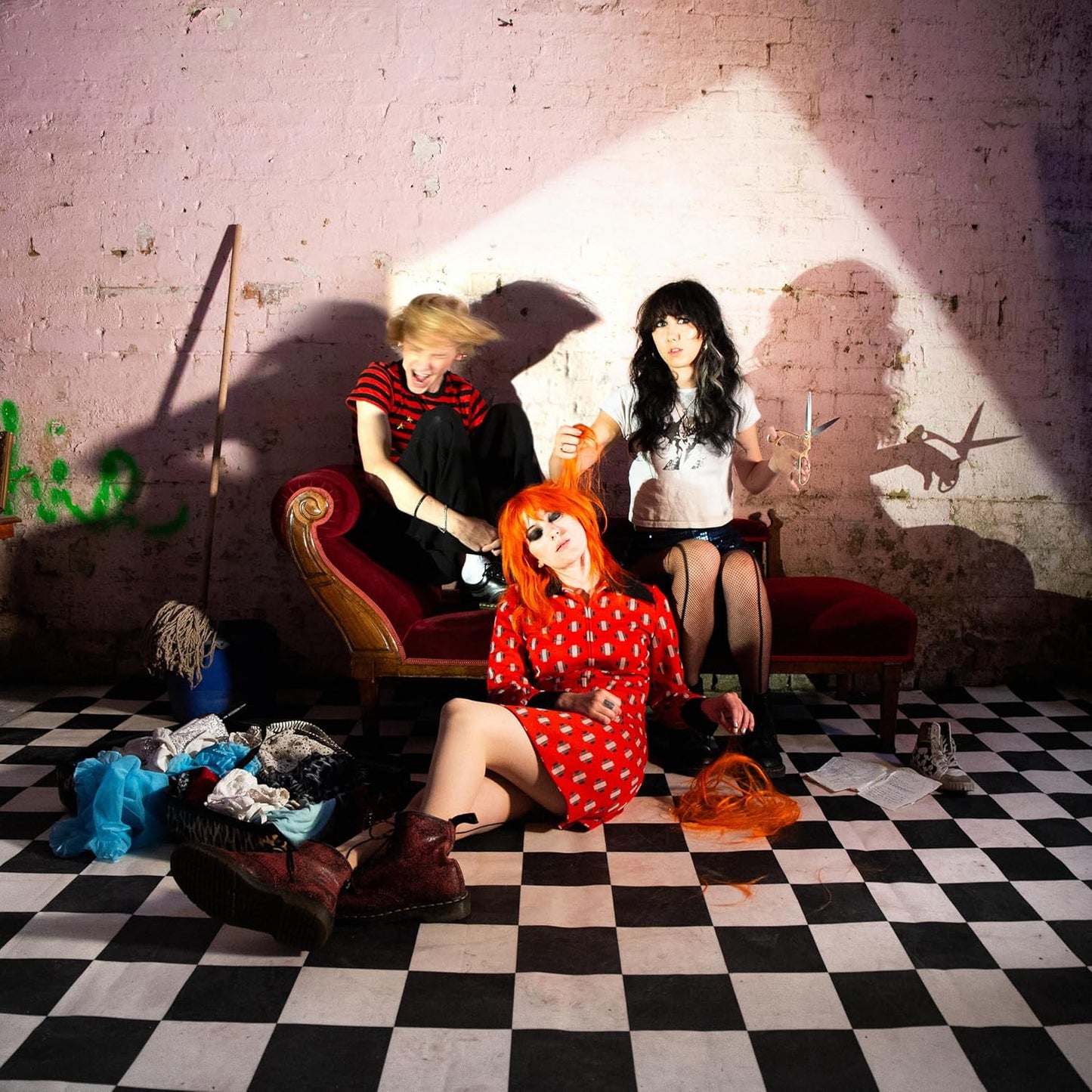Three people in vibrant clothing pose on a checkered floor.