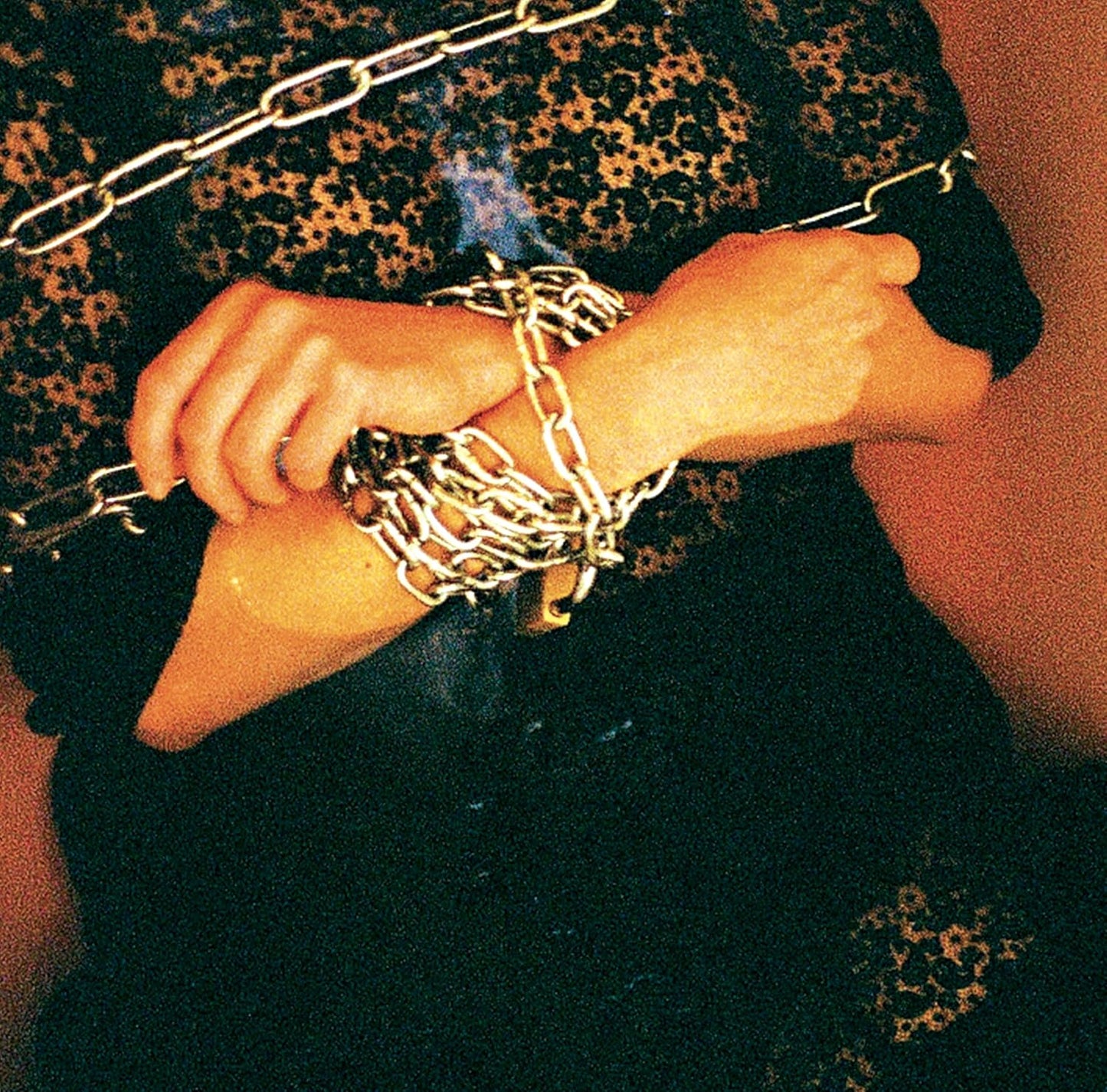 Hands gripping a metal chain against a dark, patterned background.