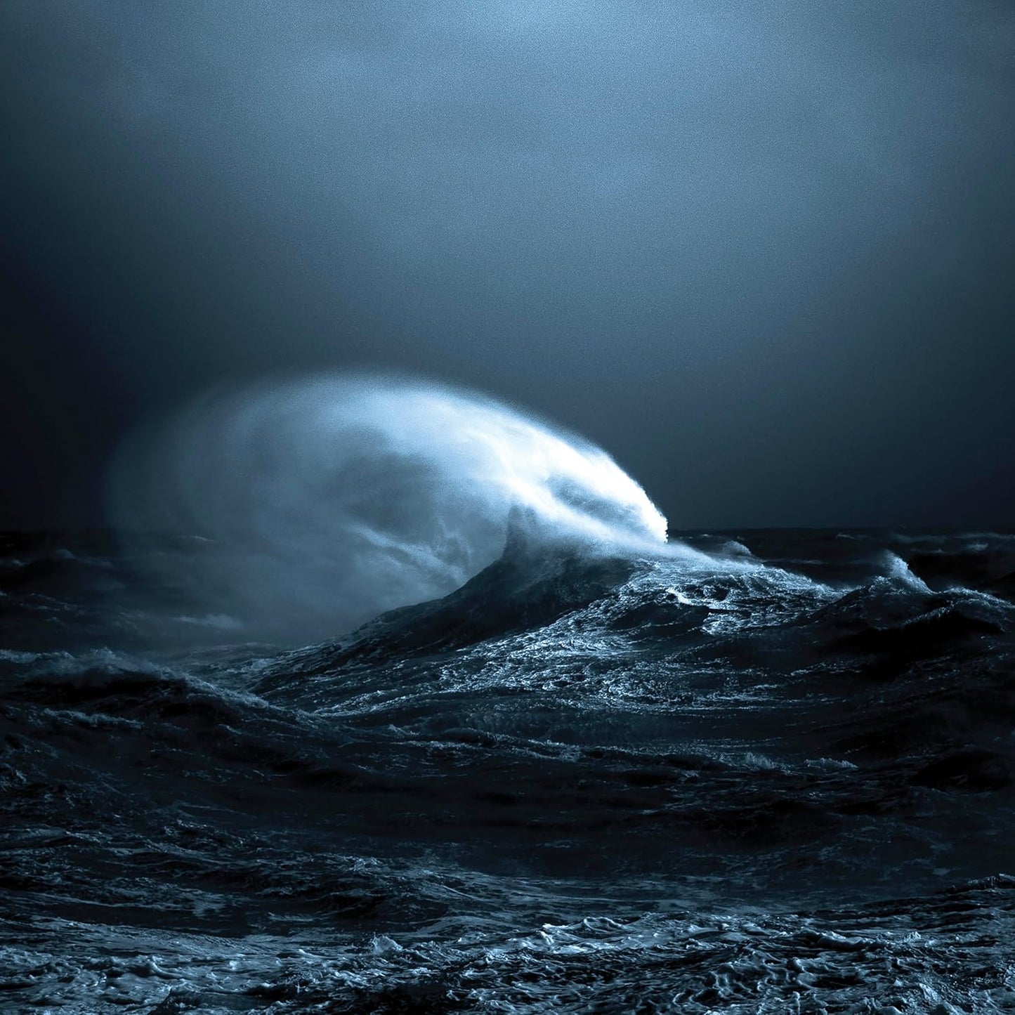 Dark blue ocean wave crashing under a stormy, cloudy sky.